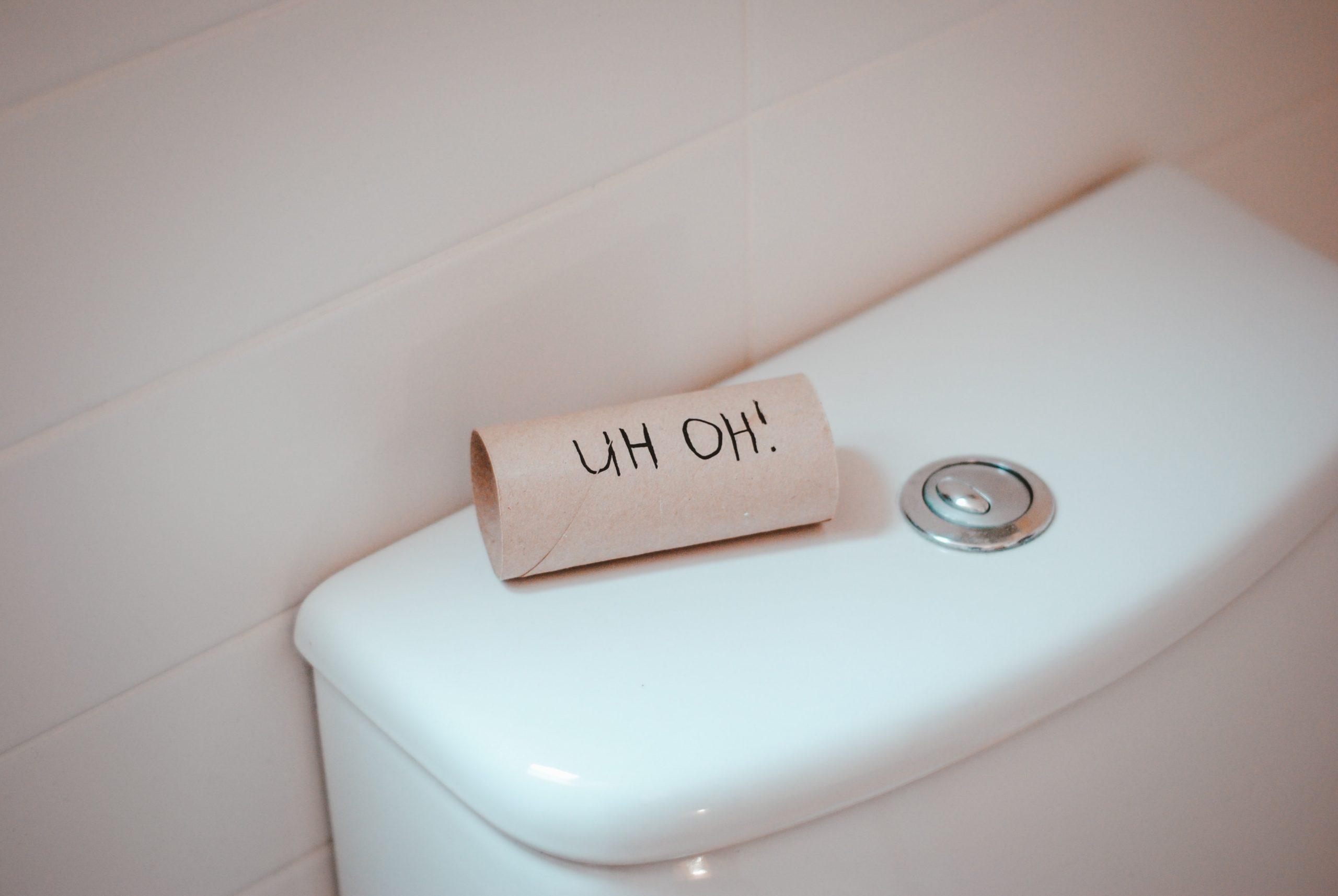 Uh oh written on an empty toilet paper roll on top of a toilet tank