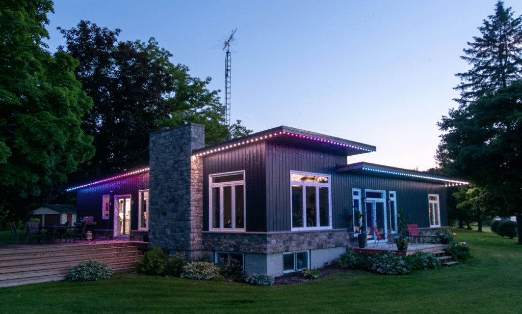 Modern home with purple and blue permanent outdoor lighting along the roofline at dusk