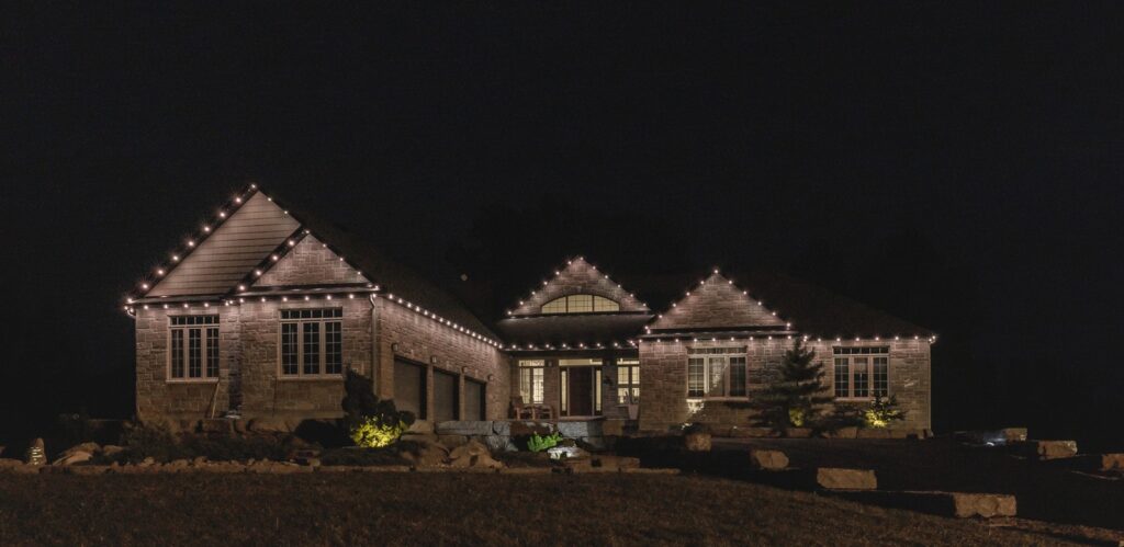 Stone home outlined in warm white permanent outdoor lighting at night