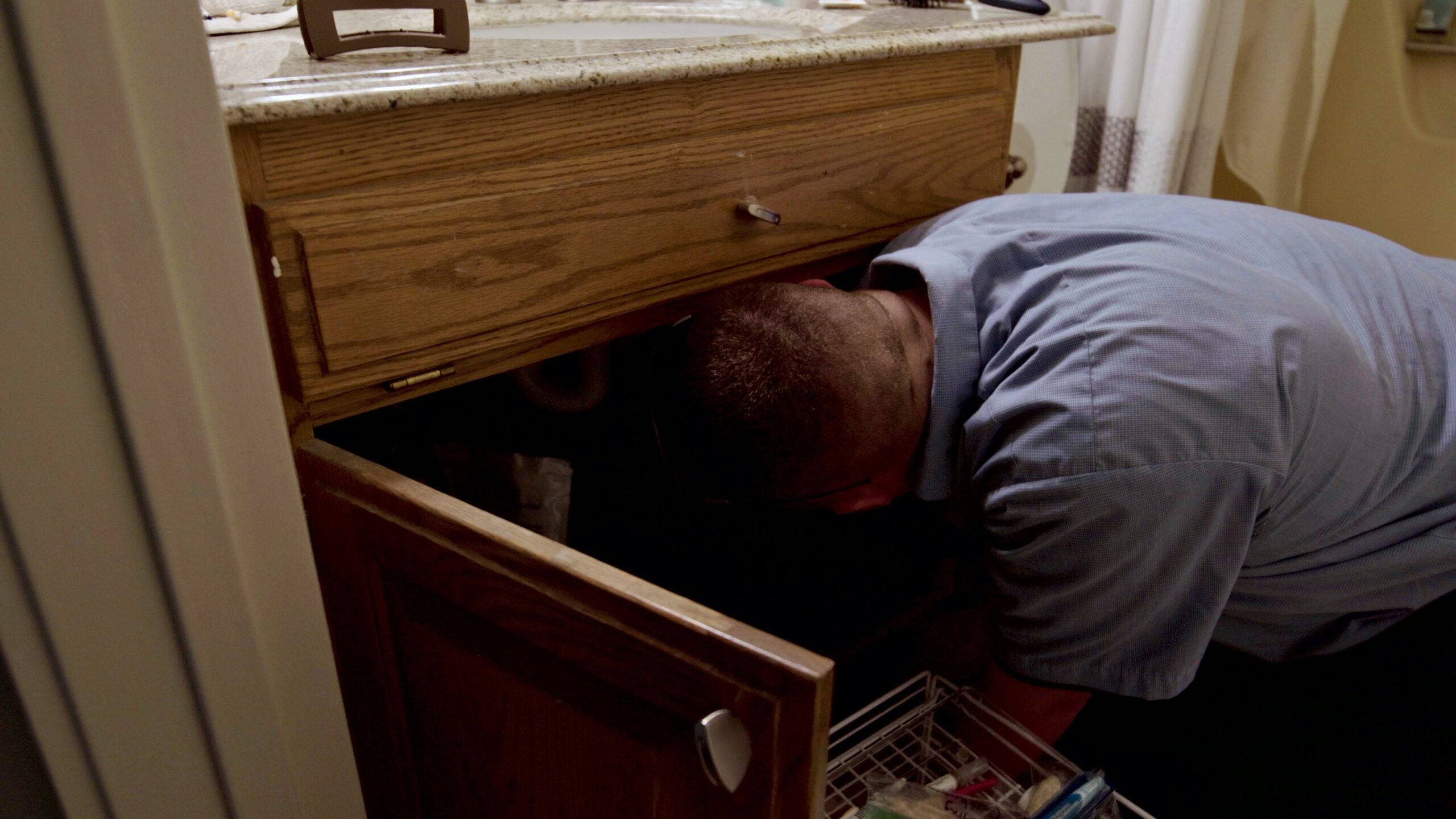 Paschal technician closing a shut-off valve under a sink while tracing a water leak in a Springdale home